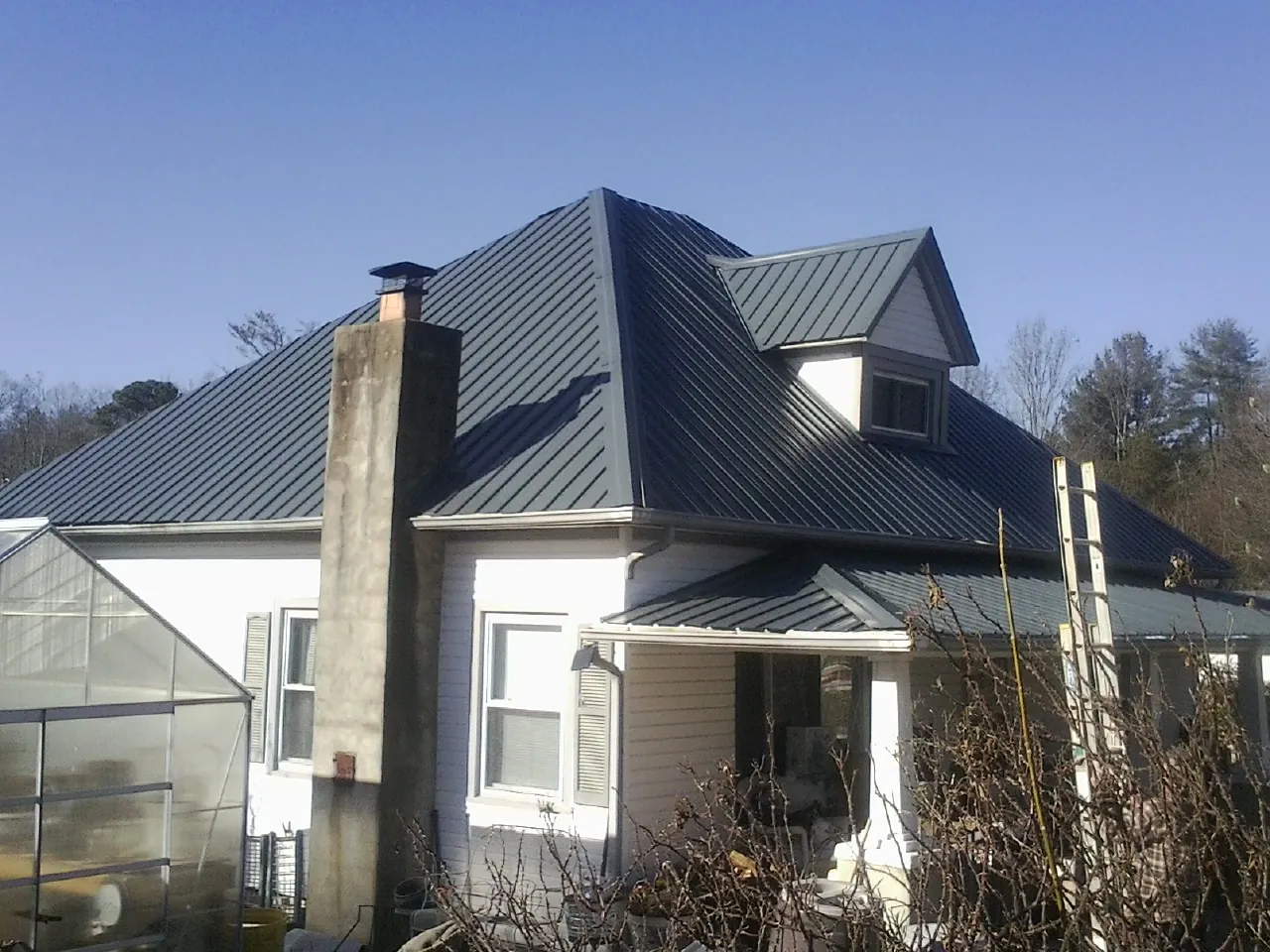 Dark blue standing seam metal roof on a white farmhouse with dormer — Slate & Tile Roof Repair by Roofing Brothers in Fairhope