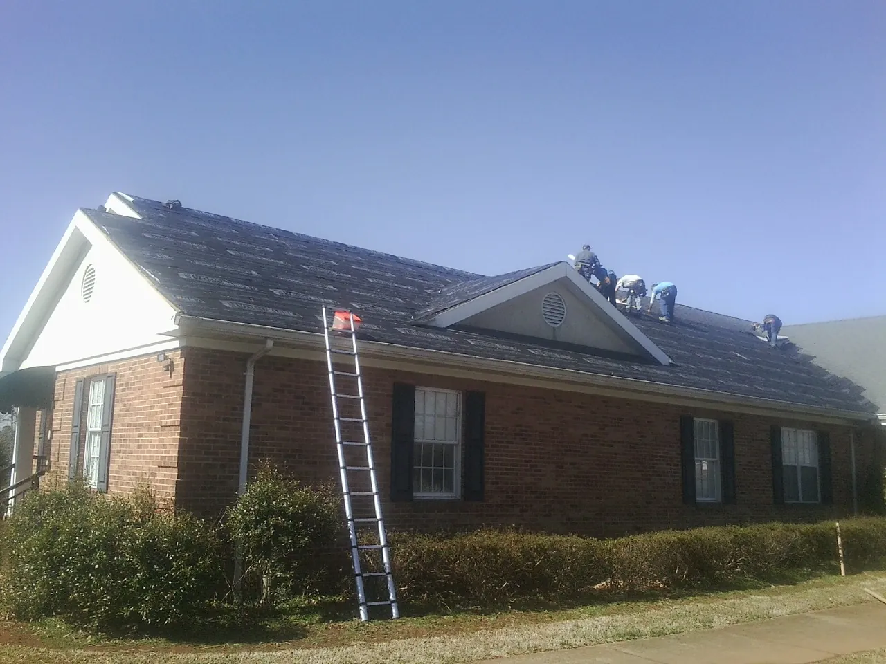 Crew tearing shingles off a brick ranch roof with a ladder set — Emergency Roof Repair work by our crew in Fairhope