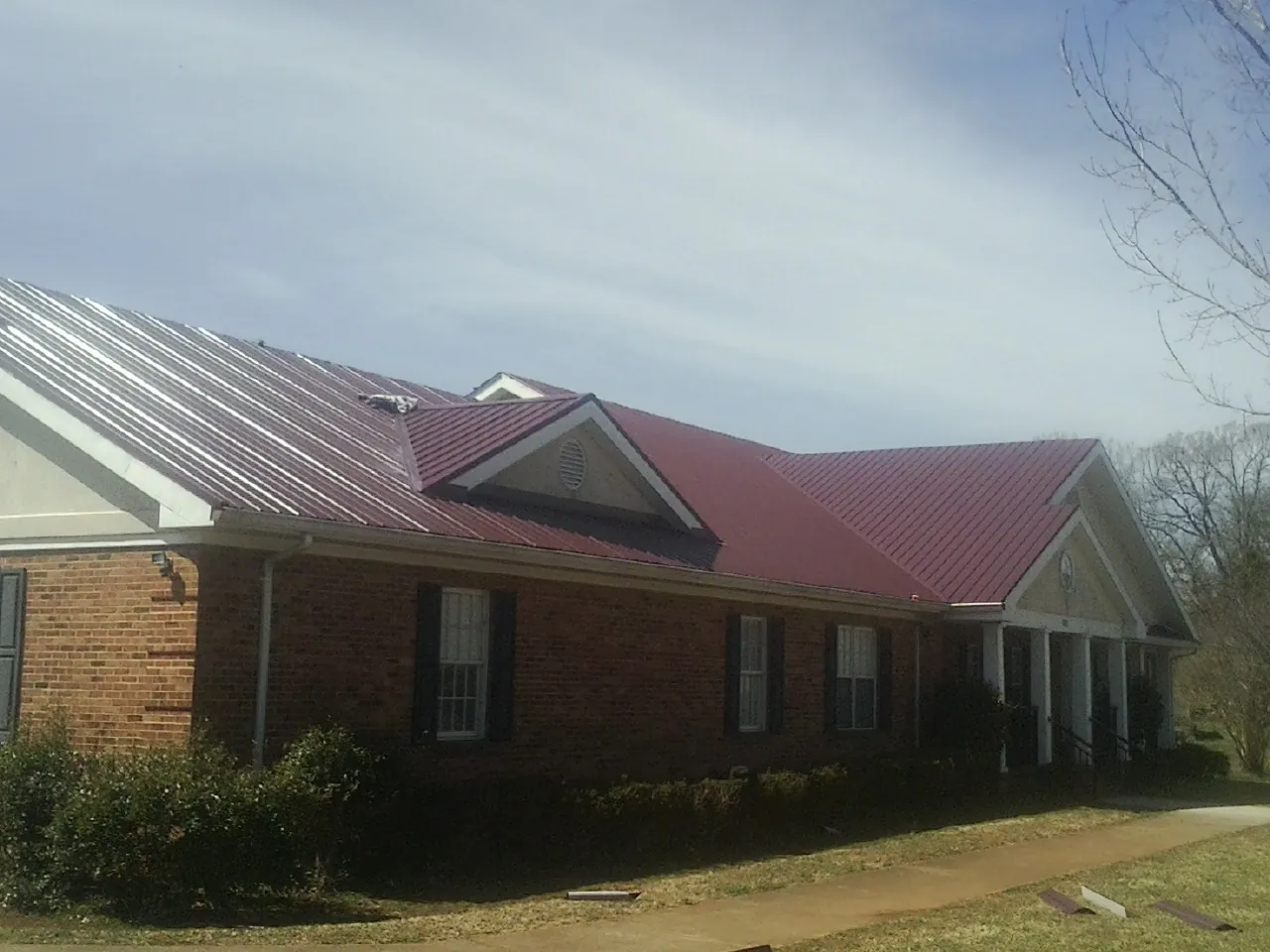 Red metal roof with gabled entries on a long brick building, from a Hail Damage Roof Repair job in Fairhope
