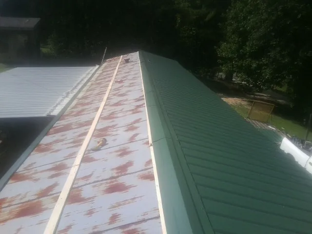 Old rusted panels beside newly installed green metal roofing — Wind Damage Roof Repair by Roofing Brothers in Fairhope