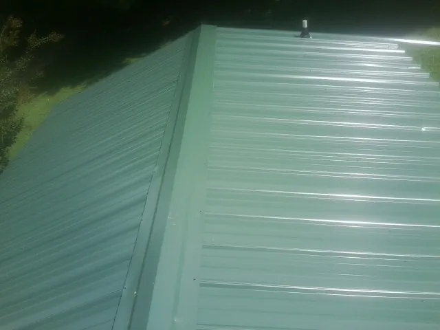 New green metal panels meeting at the ridge of a roof — Flat Roof Repair work by our crew in Fairhope